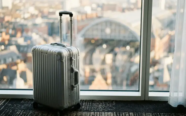 Rolling suitcase by a hotel window near a station (illustrative AI image)